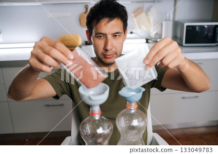 Urban farmer male pouring two different types of fertilizer from small bags into measuring cups, preparing plant nutrients in modern home kitchen. Concept of healthy sustainable cultivation Urban farmer male pouring two different types of fertilizer from small bags into measuring cups, preparing plant nutrients in modern home kitchen. Concept of healthy sustainable cultivation 133049783