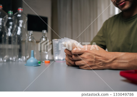 Close-up hands of gardening enthusiast wearing protective eyewear measuring nutrient solution for vertical hydroponic setup, maximizing plant health and productivity in compact indoor growing space 133049786