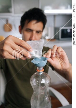 Agricultural technician male pouring organic fertilizer through funnel into plastic bottle, mixing nutrient-rich solution for healthy garden plants. Concept of healthy and sustainable cultivation 133049790