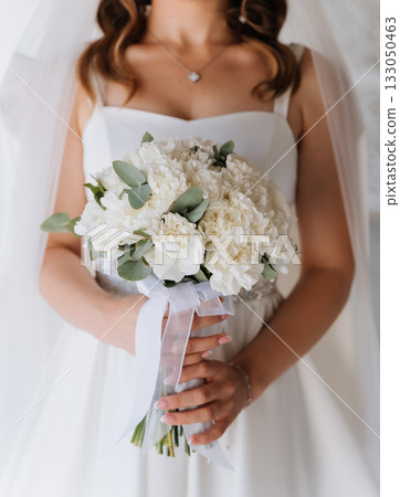 Bride holding white bouquet with ribbon in bright minimalist wedding closeup 133050463