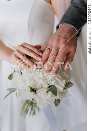 Wedding rings on couples hands over white bouquet, elegant closeup Wedding rings on couples hands over white bouquet, elegant closeup 133050468