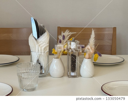 Table arrangement with cutlery, glassware, and dried flowers. Cozy minimalist cafe atmosphere, attention to detail, and warm daylight mood. 133050479