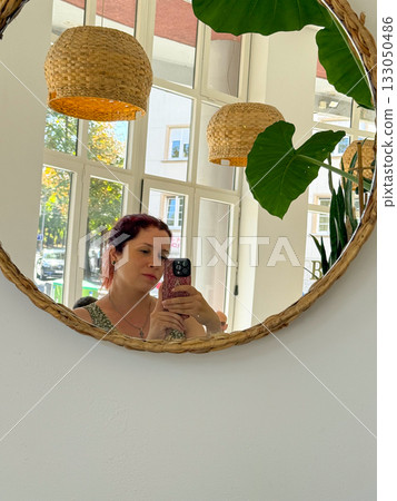 Woman taking mirror selfie in bright cafe interior. Natural light, reflection, and candid everyday lifestyle moment. 133050486