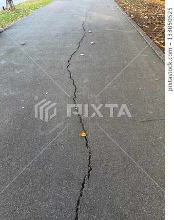 Cracked asphalt surface with visible damage lines. Urban decay, infrastructure wear, and passage of time. 133050525