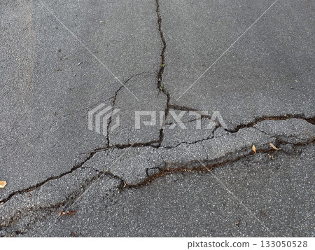 Cracked asphalt surface with visible damage lines. Urban decay, infrastructure wear, and passage of time. Cracked asphalt surface with visible damage lines. Urban decay, infrastructure wear, and passage of time. 133050528