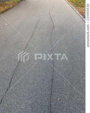 Cracked asphalt surface with visible damage lines. Urban decay, infrastructure wear, and passage of time. 133050530