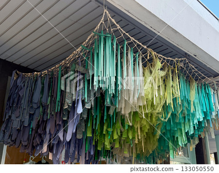 Hanging ribbons and neckties in gradient shades of green and blue. Art installation, texture, and color harmony in creative street decor. Hanging ribbons and neckties in gradient shades of green and blue. Art installation, texture, and color harmony in creative street decor. 133050550