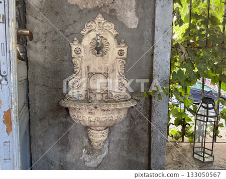Vintage stone wall fountain with ornamental detail and aged texture. Historic charm, nostalgia, and European architectural heritage preserved in everyday space. 133050567