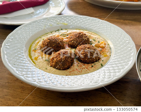 Falafel served on creamy hummus with sesame, olive oil, and spices. Middle Eastern cuisine, flavor, and healthy balance of traditional food culture. Falafel served on creamy hummus with sesame, olive oil, and spices. Middle Eastern cuisine, flavor, and healthy balance of traditional food culture. 133050574