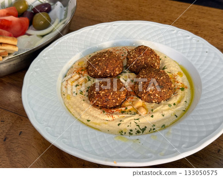 Plate of falafel served on creamy hummus with olive oil and herbs. Mediterranean cuisine, flavor, and aesthetic of healthy homemade food. 133050575