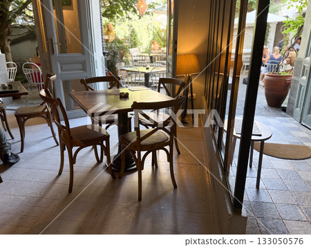 Cozy cafe interior with open doors to sunny terrace. Connection between indoor calm and outdoor life in gentle afternoon light. 133050576
