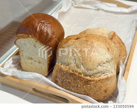 Freshly baked bread loaves in wooden tray. Rustic tradition, texture, and authenticity of natural artisan baking. Freshly baked bread loaves in wooden tray. Rustic tradition, texture, and authenticity of natural artisan baking. 133050594