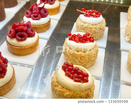Raspberry and red currant cream tartlets in pastry shop. Elegant dessert styling, harmony of fruit color, and patisserie aesthetics. Raspberry and red currant cream tartlets in pastry shop. Elegant dessert styling, harmony of fruit color, and patisserie aesthetics. 133050599
