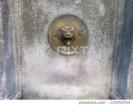 Decorative lion head fountain spout on stone wall. Historic architecture, craftsmanship, and symbolic expression of power and culture. 133050704