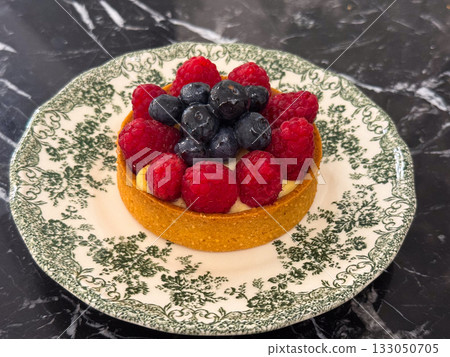 Tart with raspberries and blueberries on vintage plate. Dessert photography, patisserie aesthetics, and culinary craftsmanship with fresh summer fruits. Tart with raspberries and blueberries on vintage plate. Dessert photography, patisserie aesthetics, and culinary craftsmanship with fresh summer fruits. 133050705