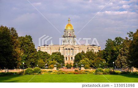 Colorado State Capitol building in Denver, Colorado. The gold dome is lit by evening sun, with a green lawn and park in the foreground under a cloudy sky 133051098