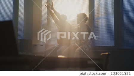 Students Sit Side by Side on Windowsill, Looking Toward Fading Daylight Filtering Through Blinds Students Sit Side by Side on Windowsill, Looking Toward Fading Daylight Filtering Through Blinds 133051521