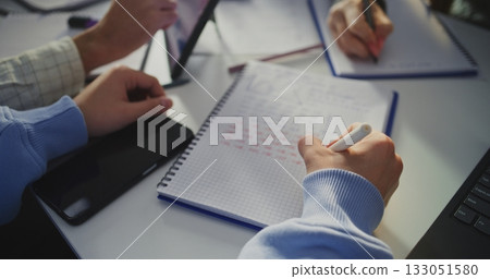 Student Writing in Notebook Next To Laptop Screen Displaying Analytical Graphs Student Writing in Notebook Next To Laptop Screen Displaying Analytical Graphs 133051580