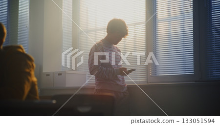 Male Student in Striped Sweatshirt Stands Near Bright Classroom Window Male Student in Striped Sweatshirt Stands Near Bright Classroom Window 133051594