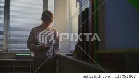 Young Man in Striped Sweater Stands by Bright Window of Lecture Hall Young Man in Striped Sweater Stands by Bright Window of Lecture Hall 133051608