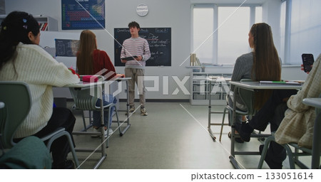 Young Male Student Stands at Front Classroom, Holding Digital Tablet While Delivering Report 133051614