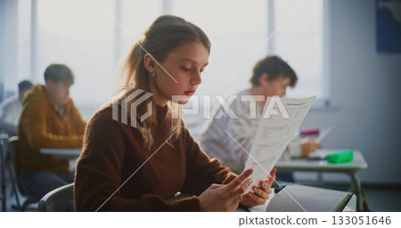 Young Female Student Smiles Brightly as Examines A Grade Report or Successful Exam Paper Young Female Student Smiles Brightly as Examines A Grade Report or Successful Exam Paper 133051646