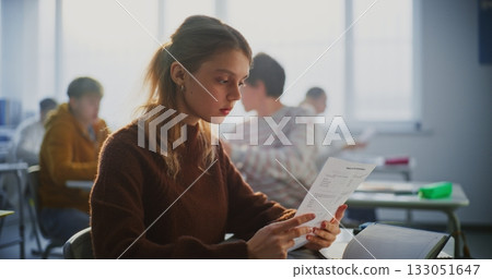 Young Female Student Smiles Brightly as Examines A Grade Report or Successful Exam Paper Young Female Student Smiles Brightly as Examines A Grade Report or Successful Exam Paper 133051647