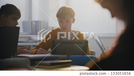 Focused Young Man Working on Tablet in Classroom, Surrounded by Classmates 133051656