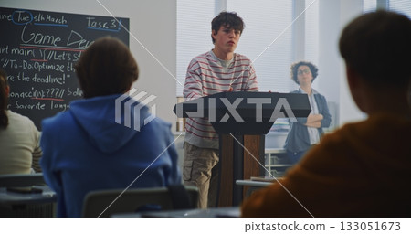 Teenage Boy at Podium Explains Work Peers, Game Dev Topic Visible on Blackboard Teenage Boy at Podium Explains Work Peers, Game Dev Topic Visible on Blackboard 133051673