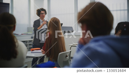 Confident Female Instructor Teaches Coding to Attentive Students, Pointing Lines Code on Display 133051684