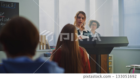 Beautiful Teenage Girl Stands Podium, Delivering Report Classmates in Bright, Modern Classroom Beautiful Teenage Girl Stands Podium, Delivering Report Classmates in Bright, Modern Classroom 133051692