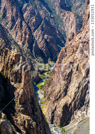 Vertical view looking down at the Gunnison River flowing through the deep, narrow Black Canyon. Steep granite cliffs cast shadows on the water Vertical view looking down at the Gunnison River flowing through the deep, narrow Black Canyon. Steep granite cliffs cast shadows on the water 133052931