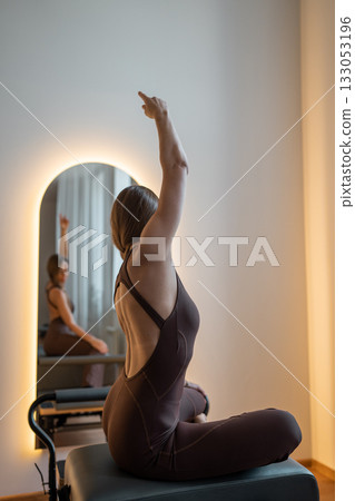 Beautiful, fit woman in sporty attire performing abdominal strength exercises on a Pilates reformer machine in a modern gym. Active training or physical rehabilitation concept image. Beautiful, fit woman in sporty attire performing abdominal strength exercises on a Pilates reformer machine in a modern gym. Active training or physical rehabilitation concept image. 133053196
