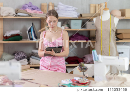 Young female dressmaker drawing in tablet in sewing workshop Young female dressmaker drawing in tablet in sewing workshop 133053466