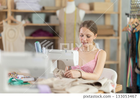 Young seamstress sews a dress on a machine Young seamstress sews a dress on a machine 133053467