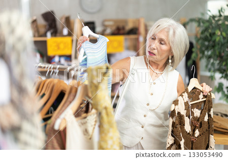 Attentive mature woman choosing something for summer in clothing store Attentive mature woman choosing something for summer in clothing store 133053490