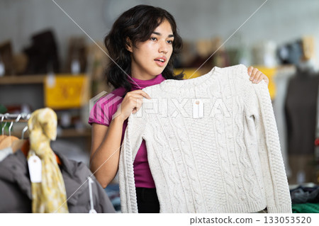 Young Filipino woman choosing sweaters in a store against the background of a Christmas tree 133053520