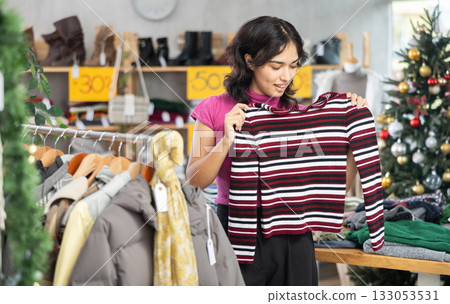 Asian woman chooses a sweater in clothing store before Christmas 133053531