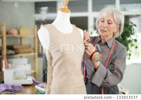 Mature female dressmaker working with mannequin in sewing workshop 133053537