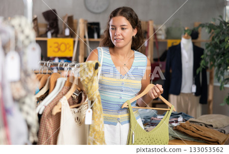 Positive young woman choosing something for summer in clothing store Positive young woman choosing something for summer in clothing store 133053562