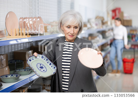 Smiling elderly woman choosing ceramic Asian style plates in store 133053566