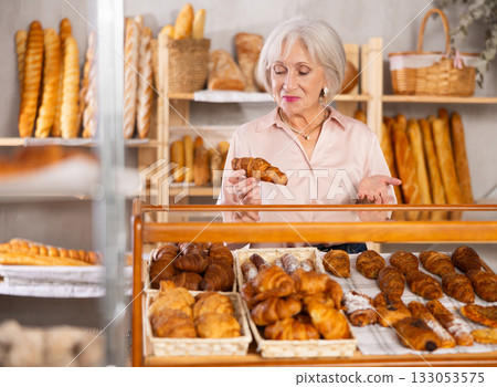 Mature woman in casual clothes chooses fresh croissants for breakfast in bakery 133053575