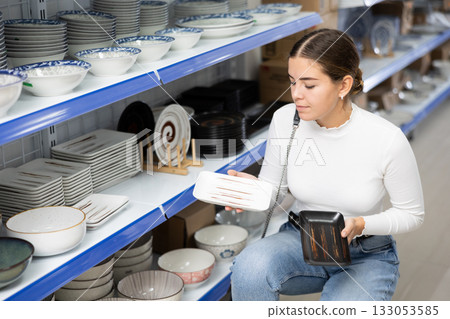 Young girl choosing square ceramic plates on shelves at Asian store 133053585