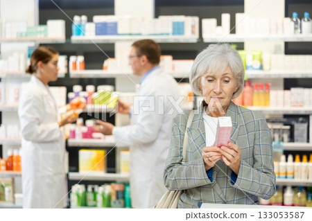 Elderly female shopper chooses a medicinal ointment in pharmacy 133053587