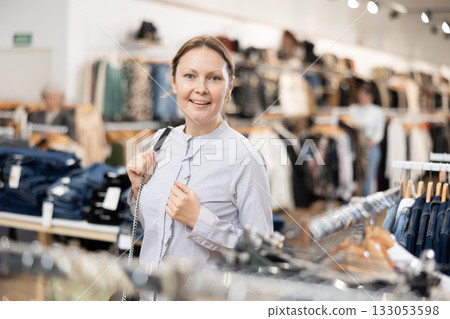 Portrait of joyful woman looking for fashionable clothes in clothing boutique 133053598