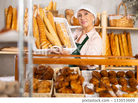 Senior female baker worker sells baguette, shows many products 133053609