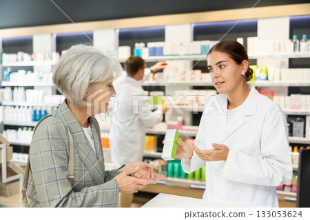Girl apothecary hold package with cream and talks with senior woman client about nuances of care Girl apothecary hold package with cream and talks with senior woman client about nuances of care 133053624
