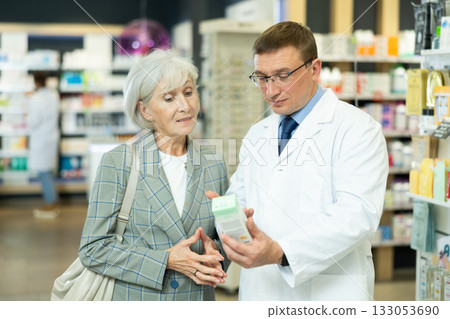 Man apothecary hold package with cream and talks with senior woman client about nuances of care 133053690