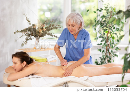 Skilled aged masseuse doing back pain relief massage to young woman 133053704