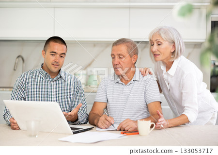Salesman seller shows on laptop details of purchase to elderly couple. Salesman seller shows on laptop details of purchase to elderly couple. 133053717